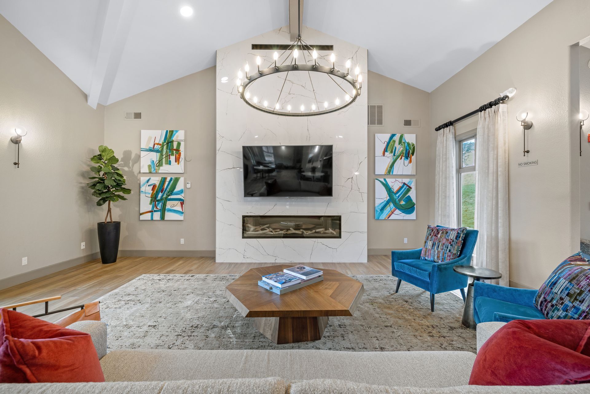 Living room with fireplace, TV, and blue armchairs, with a large rug and neutral walls at Montrachet apartments in Lakewood, CO.