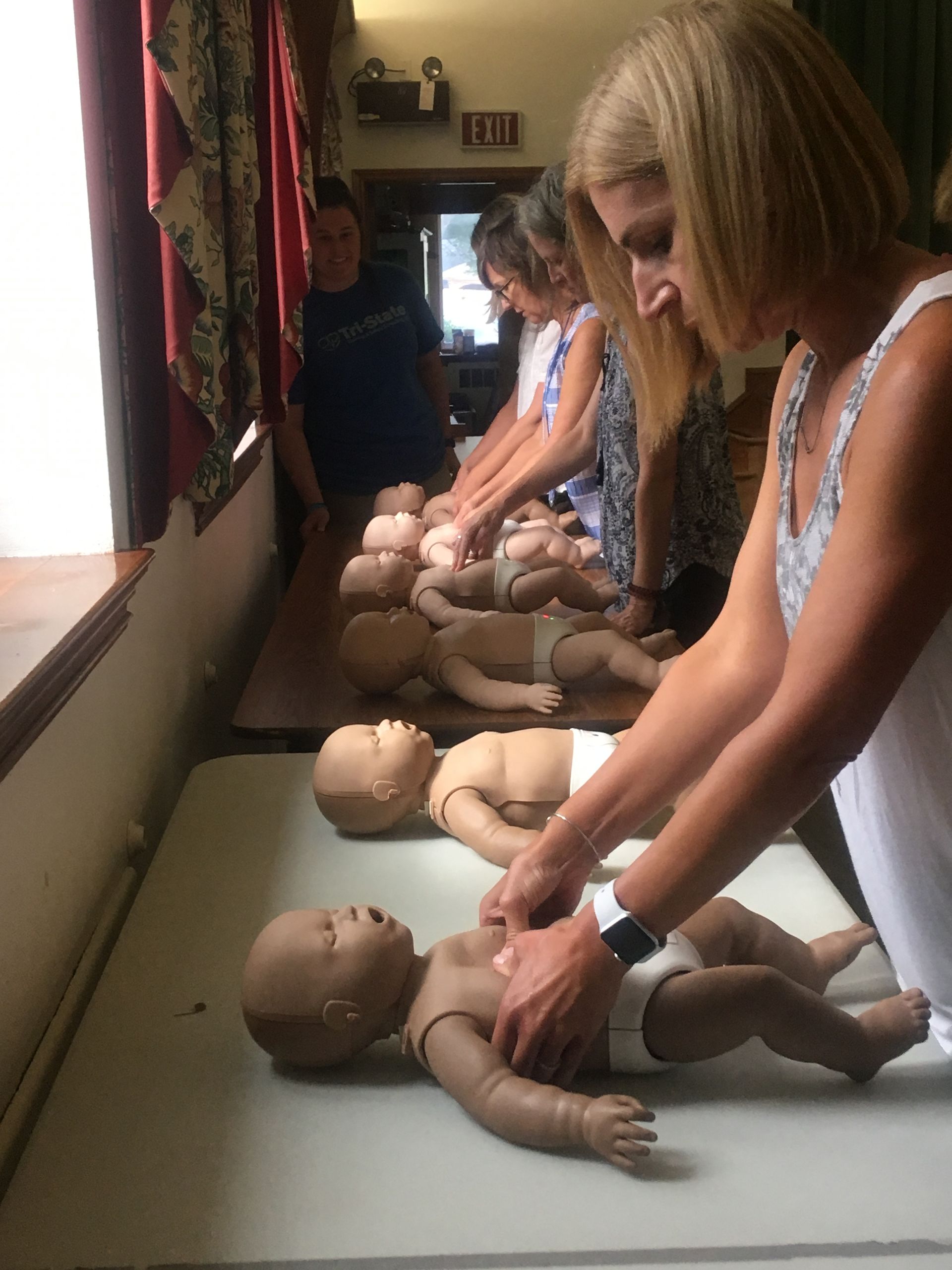 Woman demonstrating CPR on infant mannequins in a training room