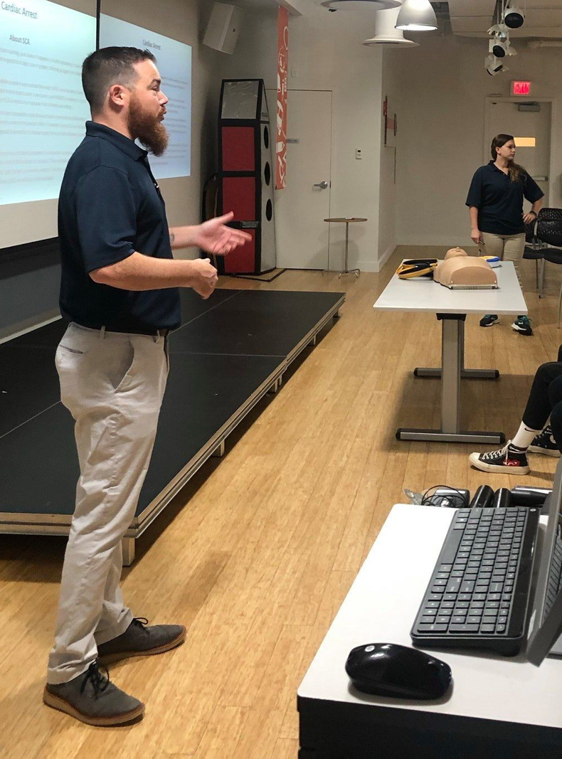 Tr-State owner Kevin Kerns speaking in a classroom beside a projected slide, with tables and computers in the foreground