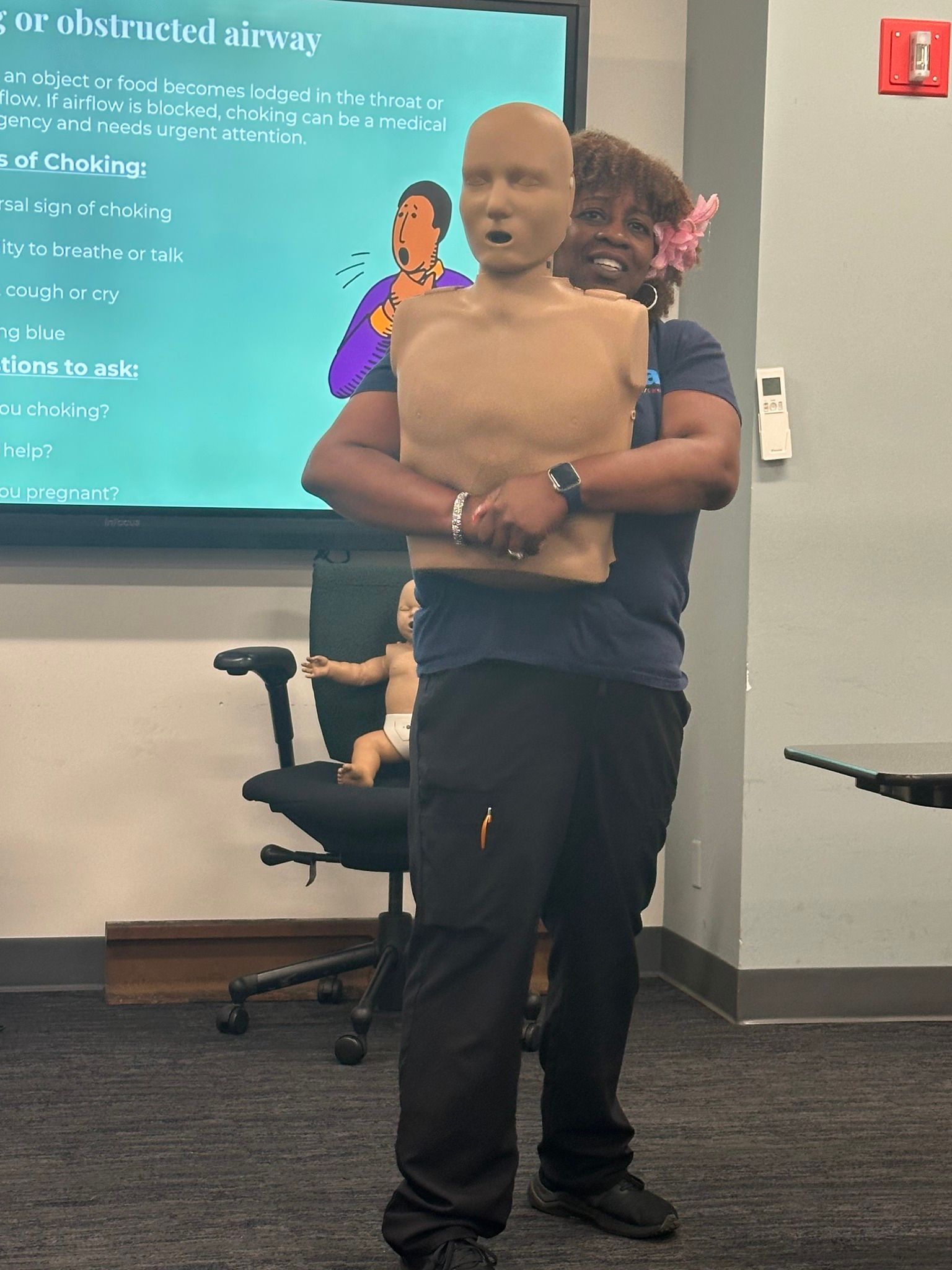 A Tri-State Training CPR instructor standing in a classroom holding a CPR mannequin