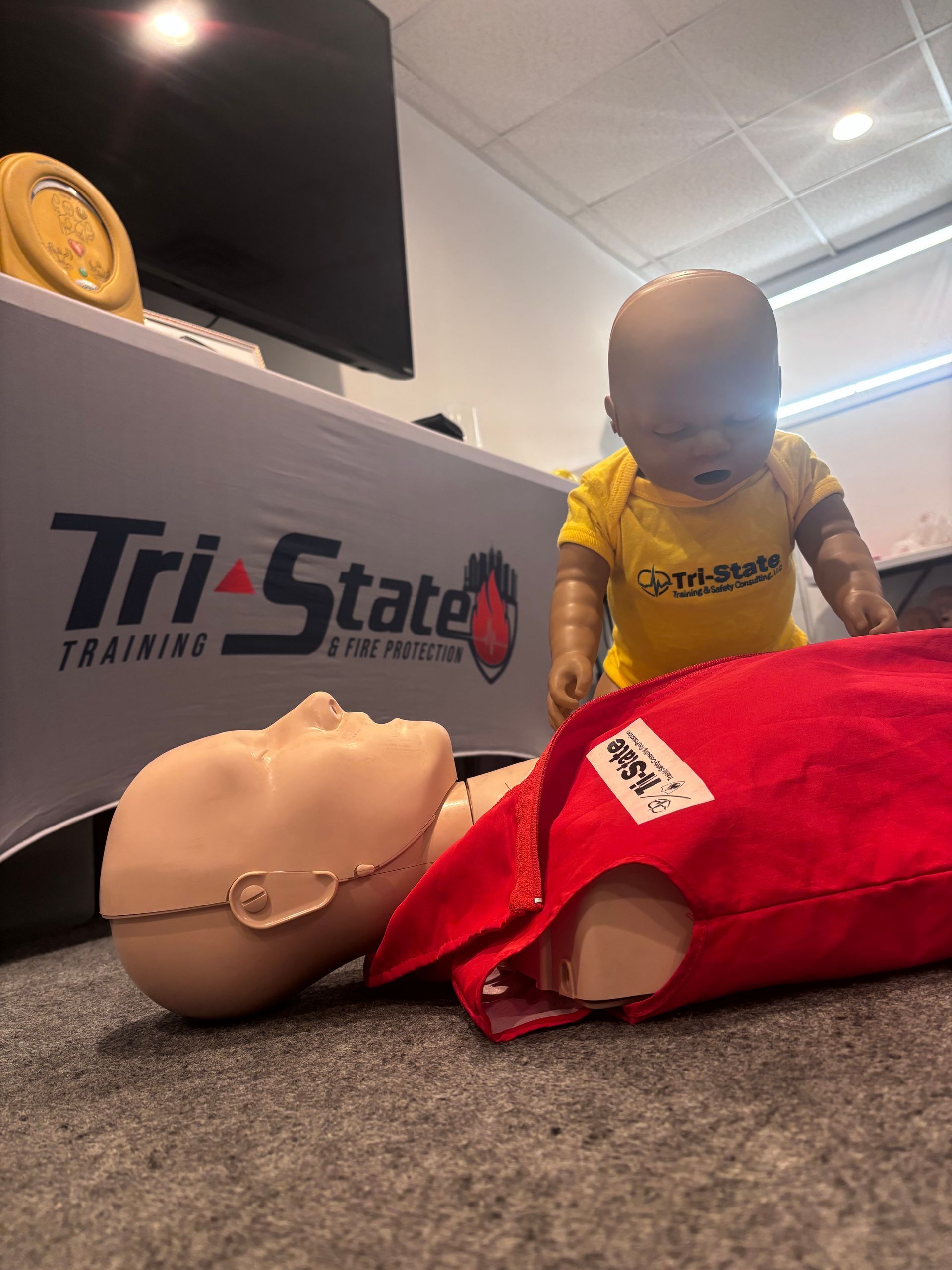 CPR manikin on carpet with an infant CPR manikin on top in a training room