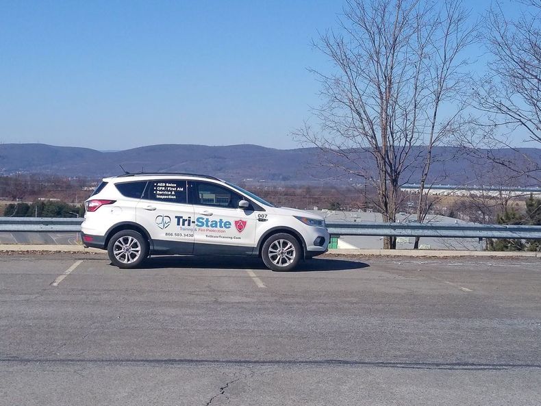White Tri-State SUV parked by roadside railing with mountains in the background