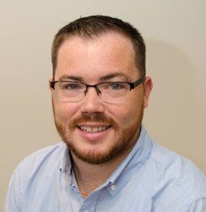 Tri-State Founder smiling with glasses and a short beard in a light blue shirt against a beige background
