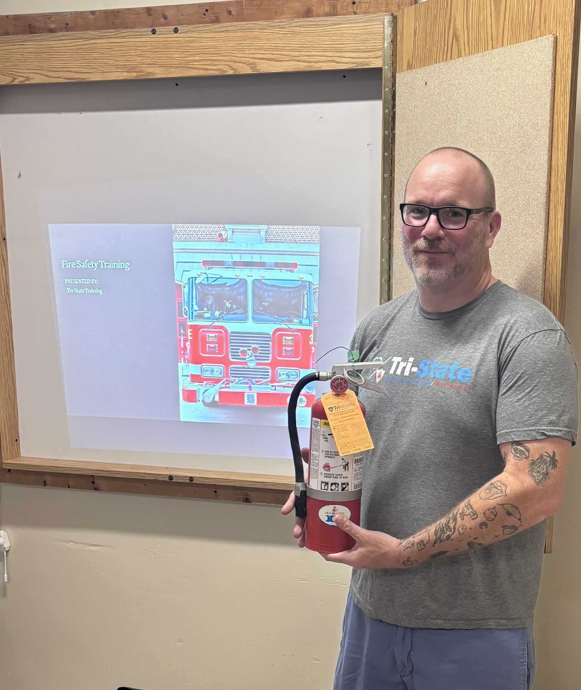 Man holding a red fire extinguisher beside a projected screen in a workshop room