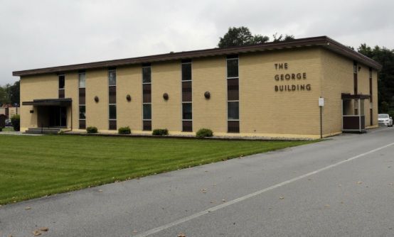 Tan brick George Building beside a road, with grass lawn and cloudy sky