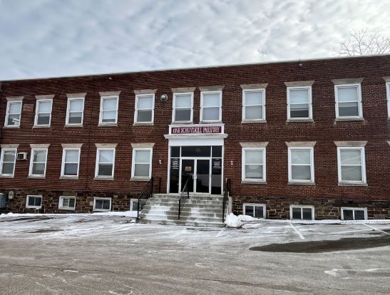 Brick two-story building with central entrance, steps, snow-covered ground, and a sign above the door.