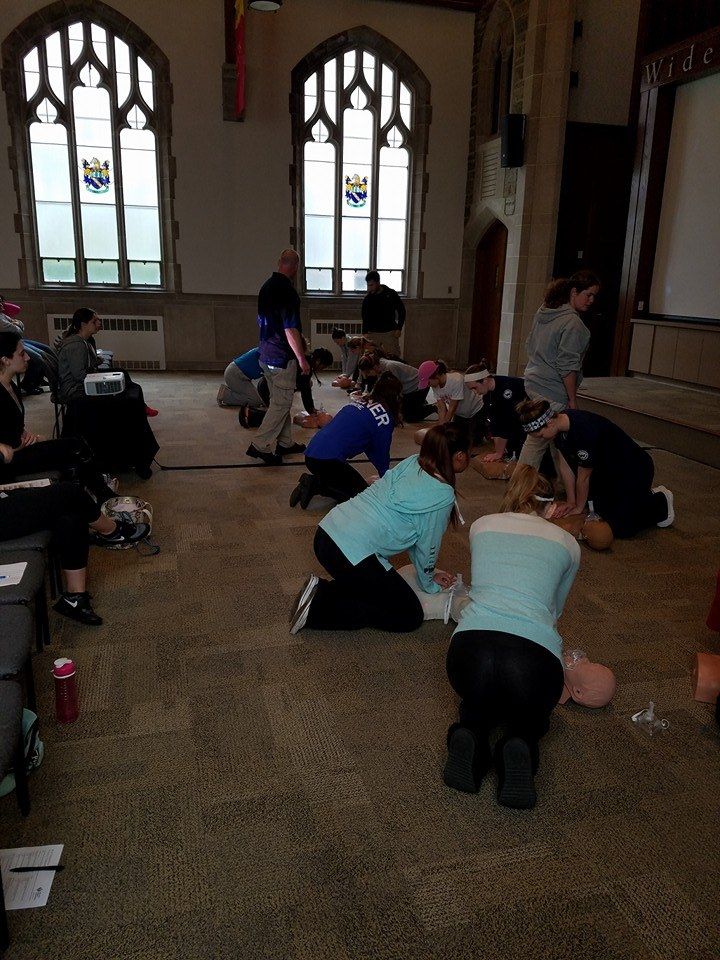 People kneeling on a church floor, practicing CPR in small groups near tall stained-glass windows.