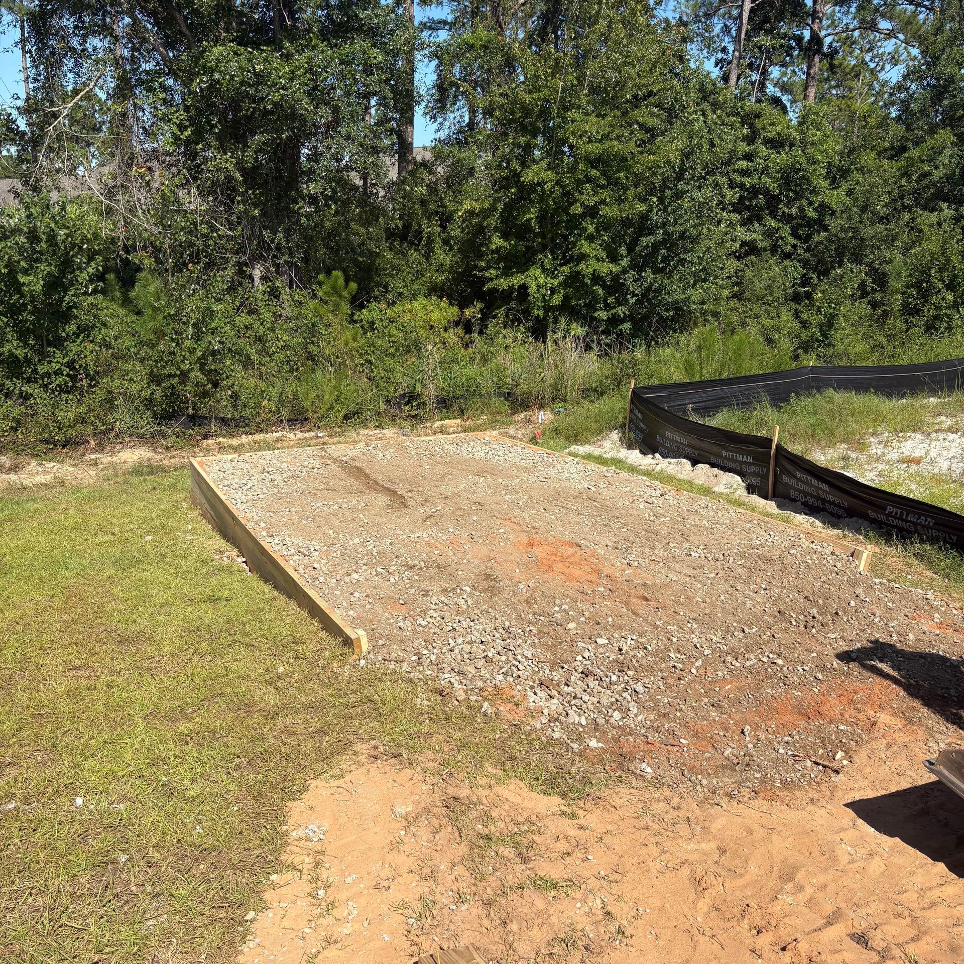 Gravel path under construction beside a grassy yard and trees, with black edging on one side