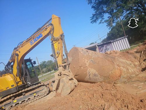 Yellow excavator digging a large dirt pile at a construction site under a blue sky.
