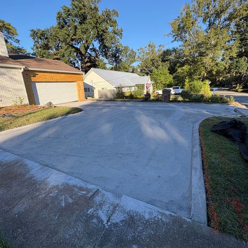 Residential driveway and garage under a clear blue sky, with trees and parked vehicles in the background