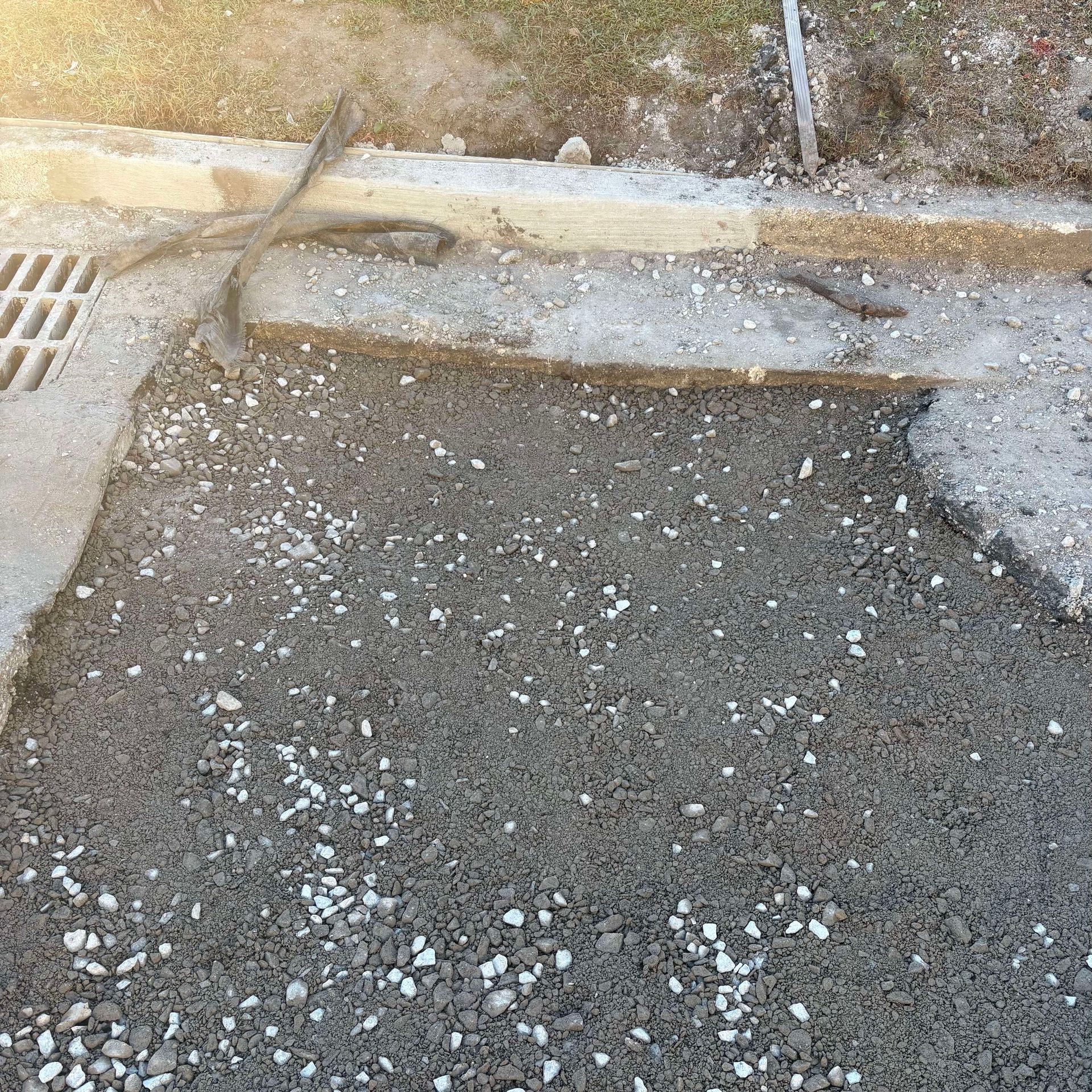 Cracked asphalt patch beside a curb and drain in an outdoor area