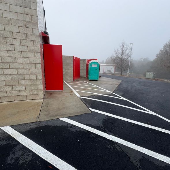 Foggy parking lot beside a brick building, with red doors, a portable toilet, and fresh white parking lines