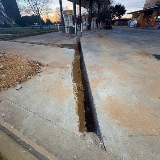 Deep open crack splits a concrete driveway at dusk near a building and street