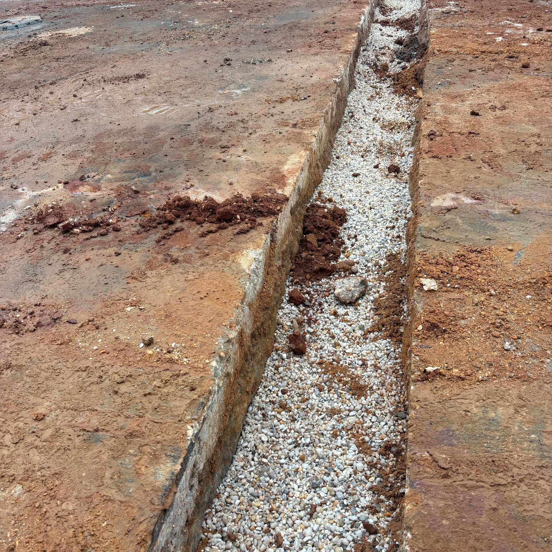 Close-up of a concrete curb drain filled with gravel, running through a dirt surface.