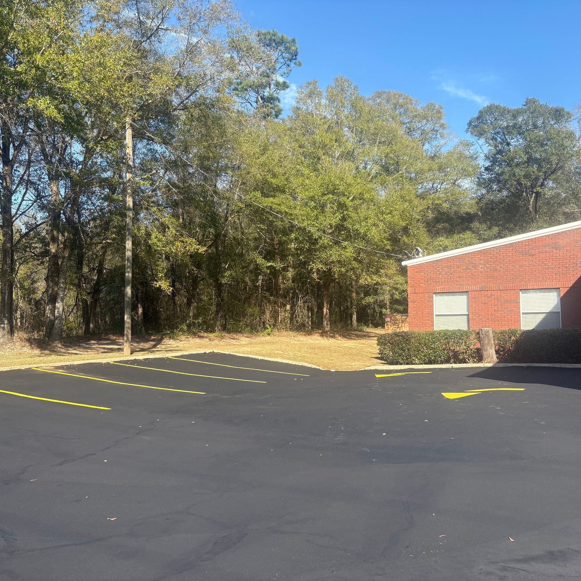 Empty parking lot beside a red brick building and wooded trees under a clear blue sky
