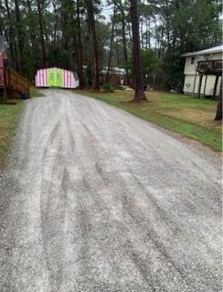 Gravel driveway curving through trees toward a pink-and-white shed beside a house