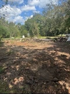 Cleared dirt lot bordered by trees under a blue sky with scattered clouds