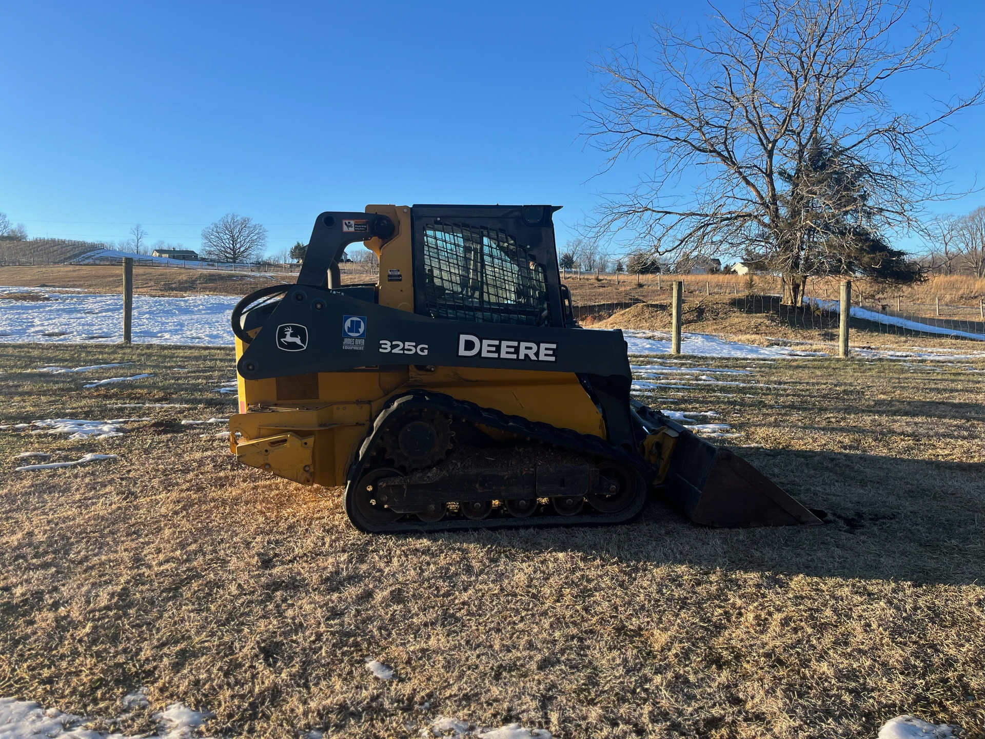 A yellow and black deere skid steer is parked in a snowy field.