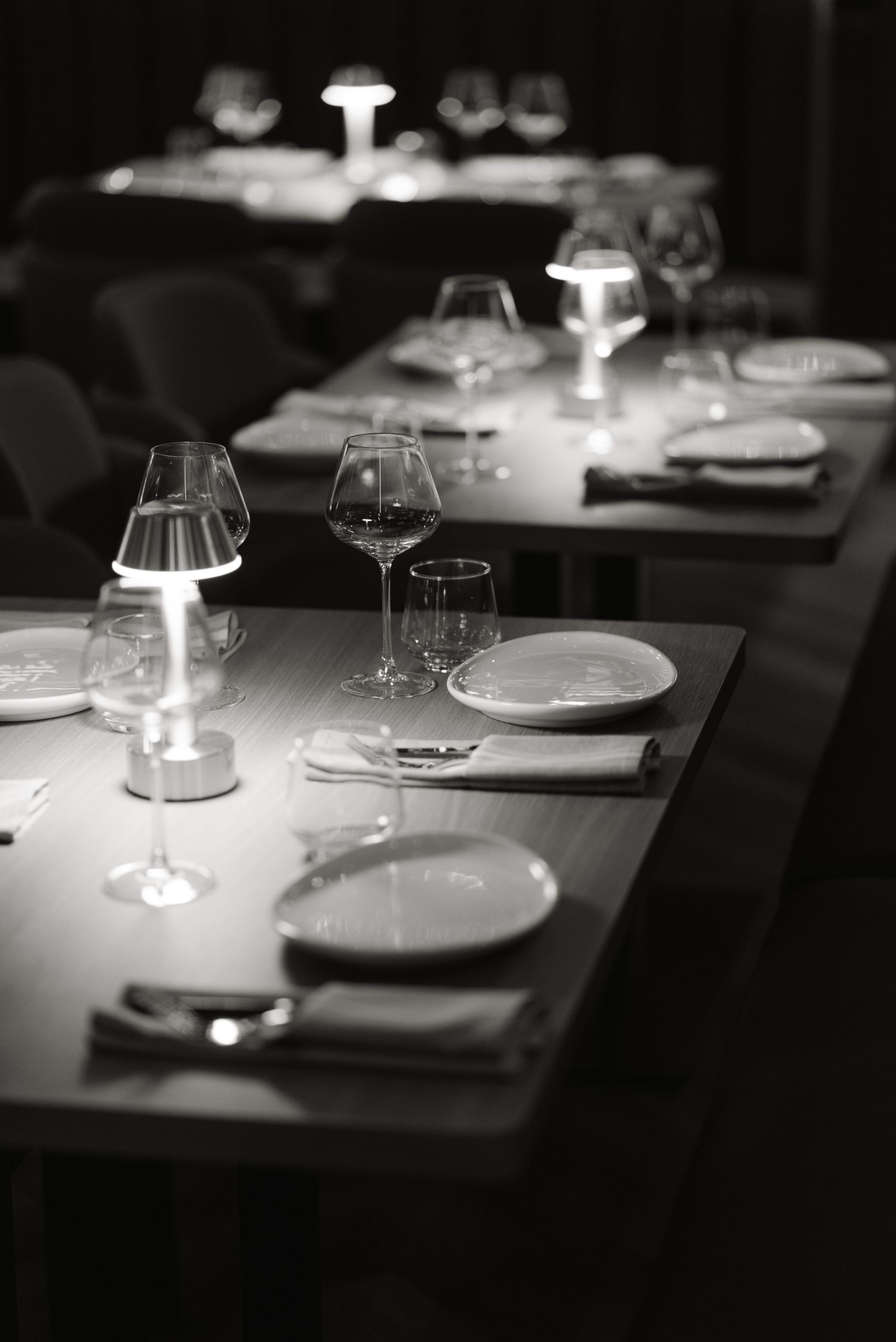 A black and white photo of a restaurant table set with plates , glasses and lamps.