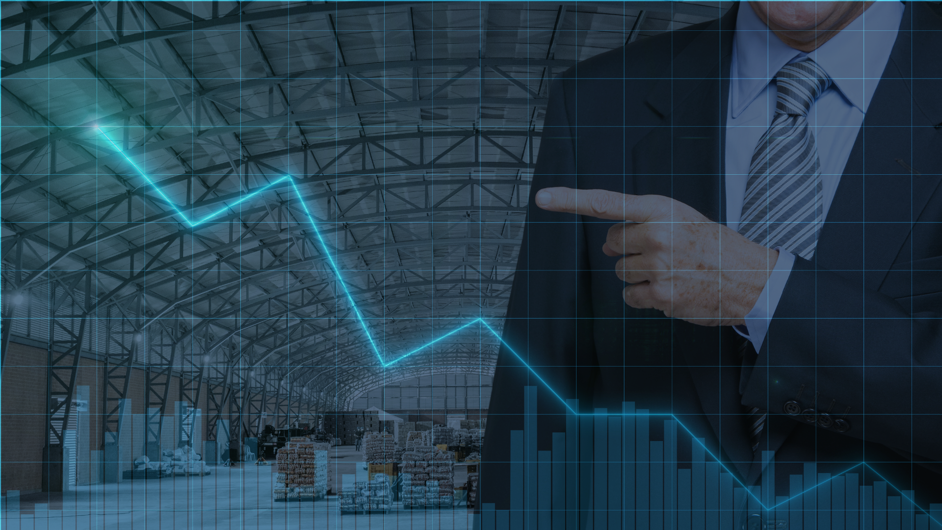 A man in a suit and tie is pointing at a graph in a warehouse.
