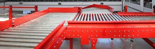 A conveyor belt in a warehouse with a red railing.