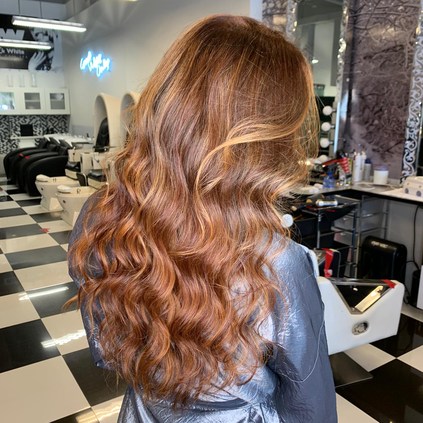 A woman with long brown hair is standing in a hair salon.