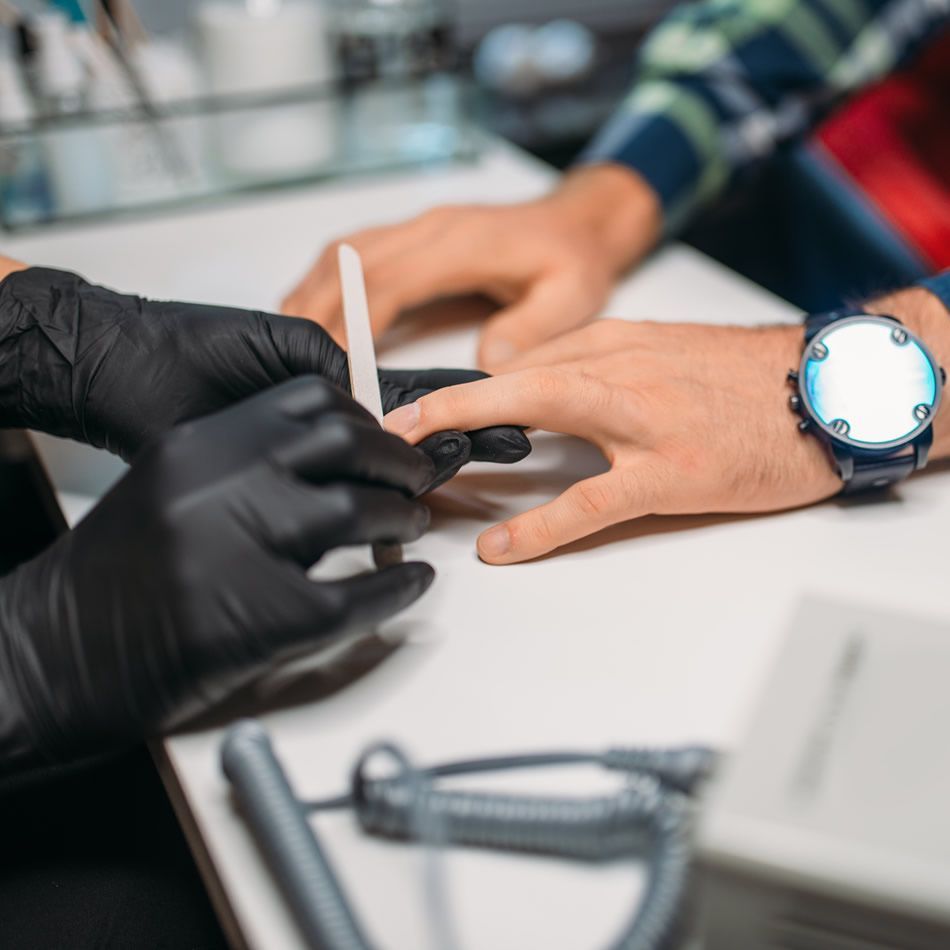 A man is getting his nails done by a woman wearing black gloves and a watch.