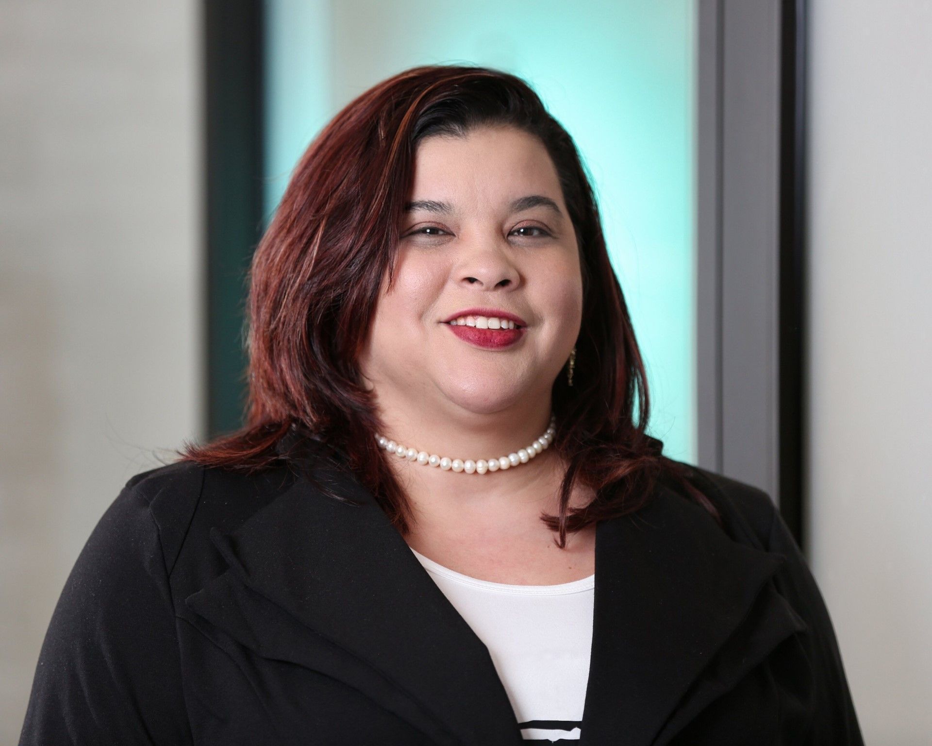 A woman wearing a black jacket and a pearl necklace is smiling for the camera.