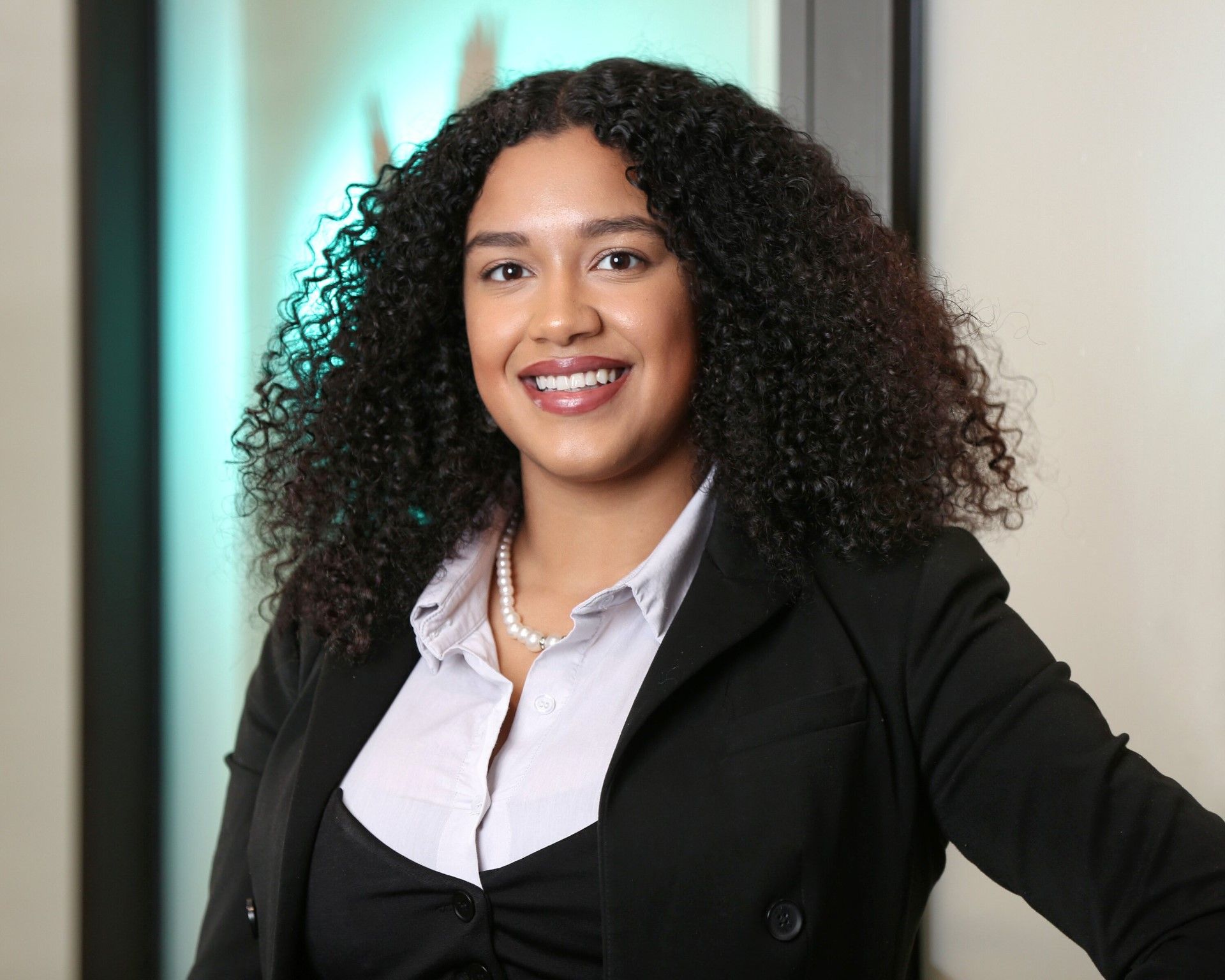A woman with curly hair is wearing a black jacket and a white shirt.