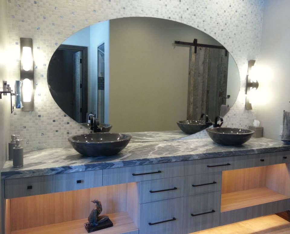 Bathroom with oval mirror, vessel sinks, and wood cabinet with under-lighting. Barn door and mosaic tile accent.