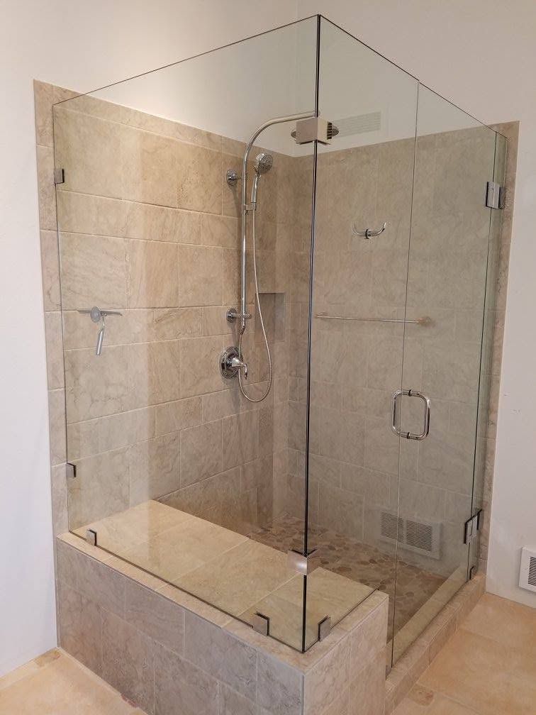 Glass-enclosed shower with beige tile walls, a built-in bench, and silver fixtures.