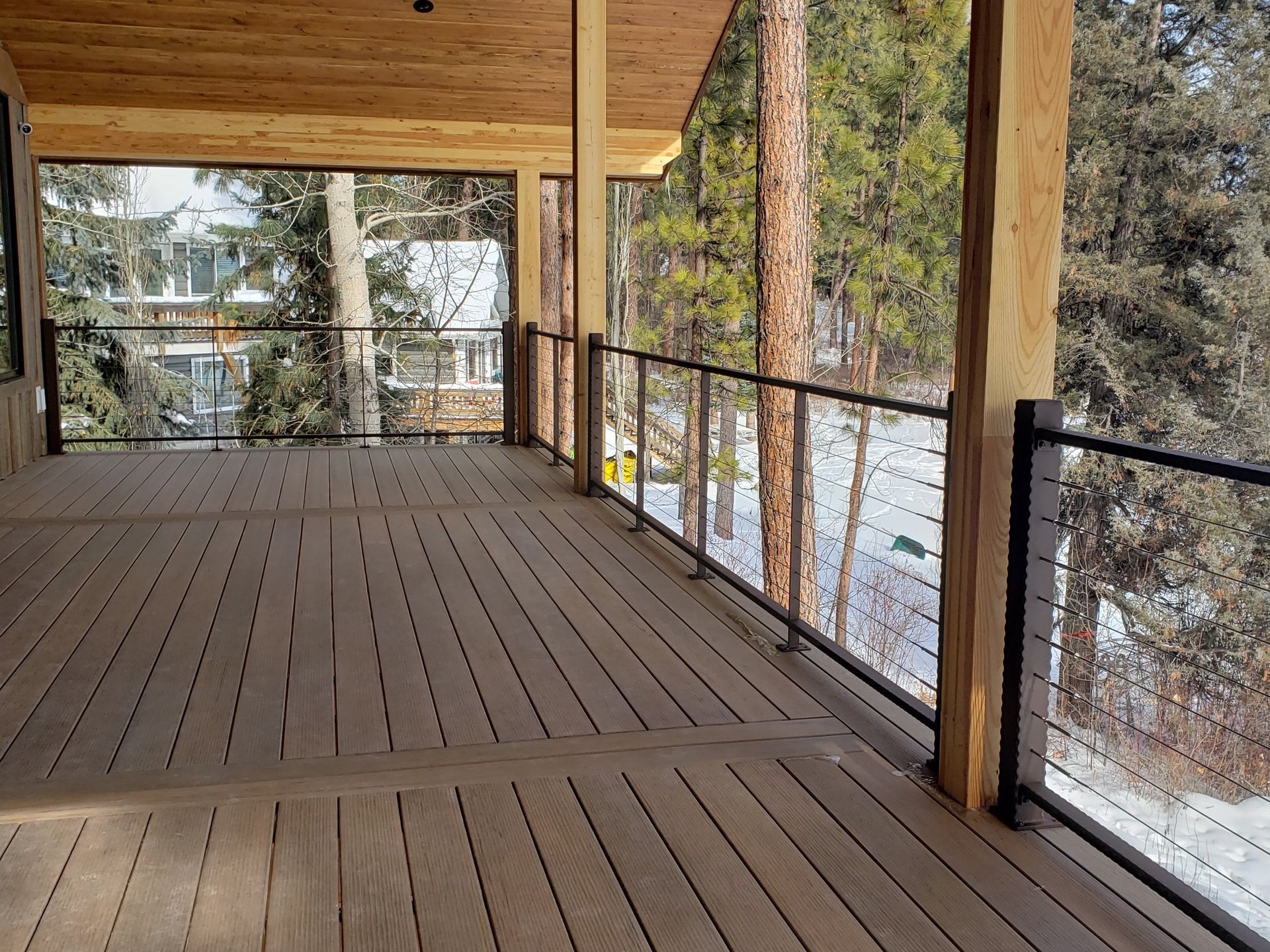 Wooden deck with cable railing, overlooking a snowy forest.