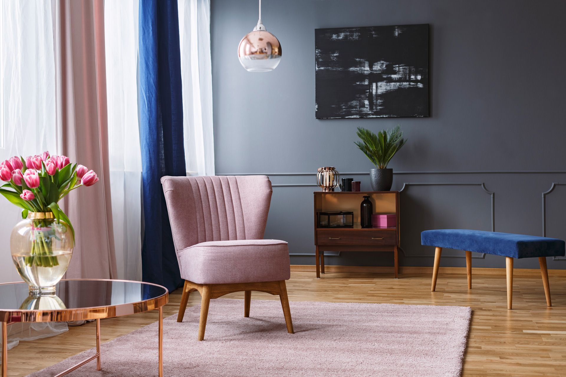 A living room with a pink chair , a table , and a vase of flowers.