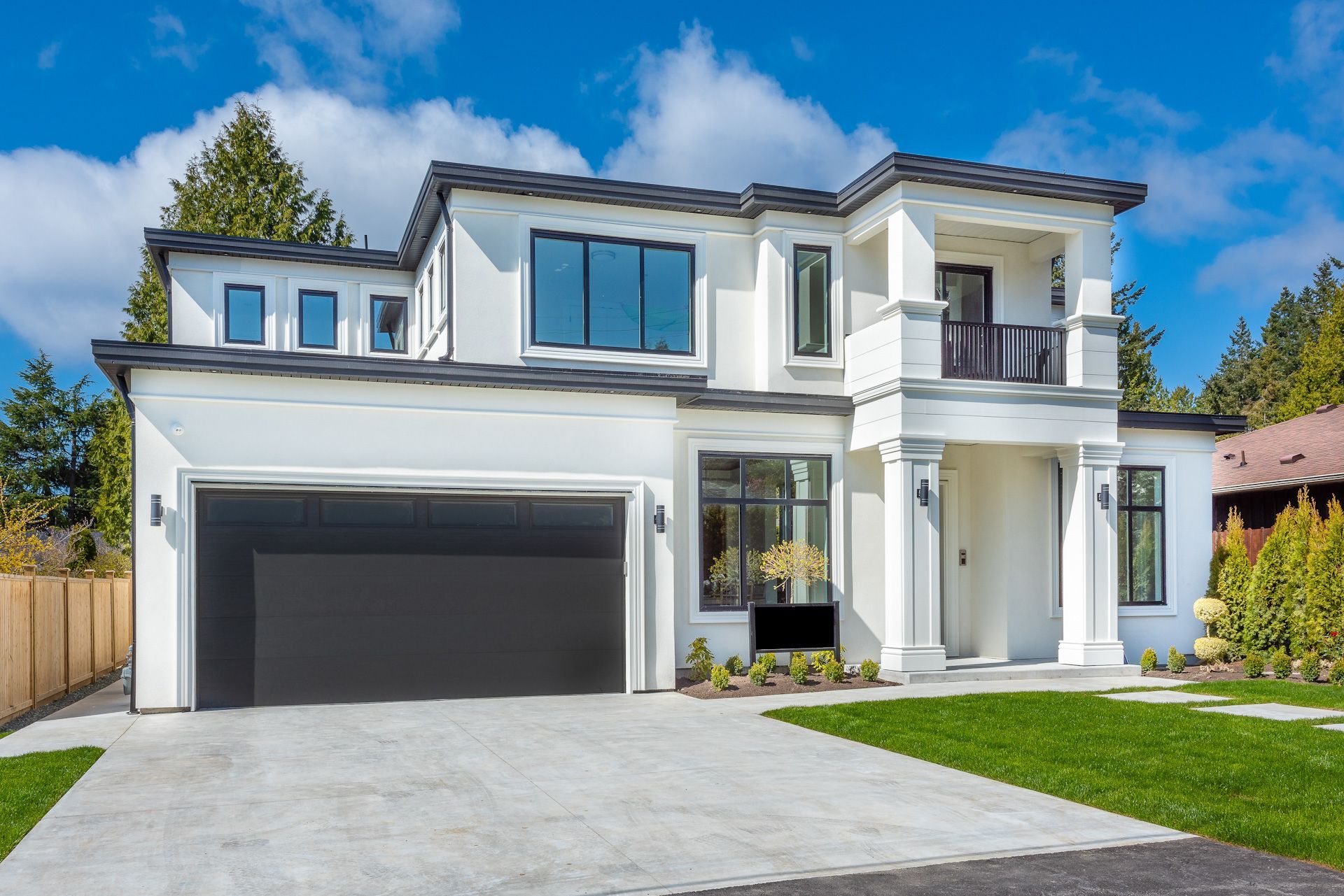 A large white house with a black garage door and a large driveway.