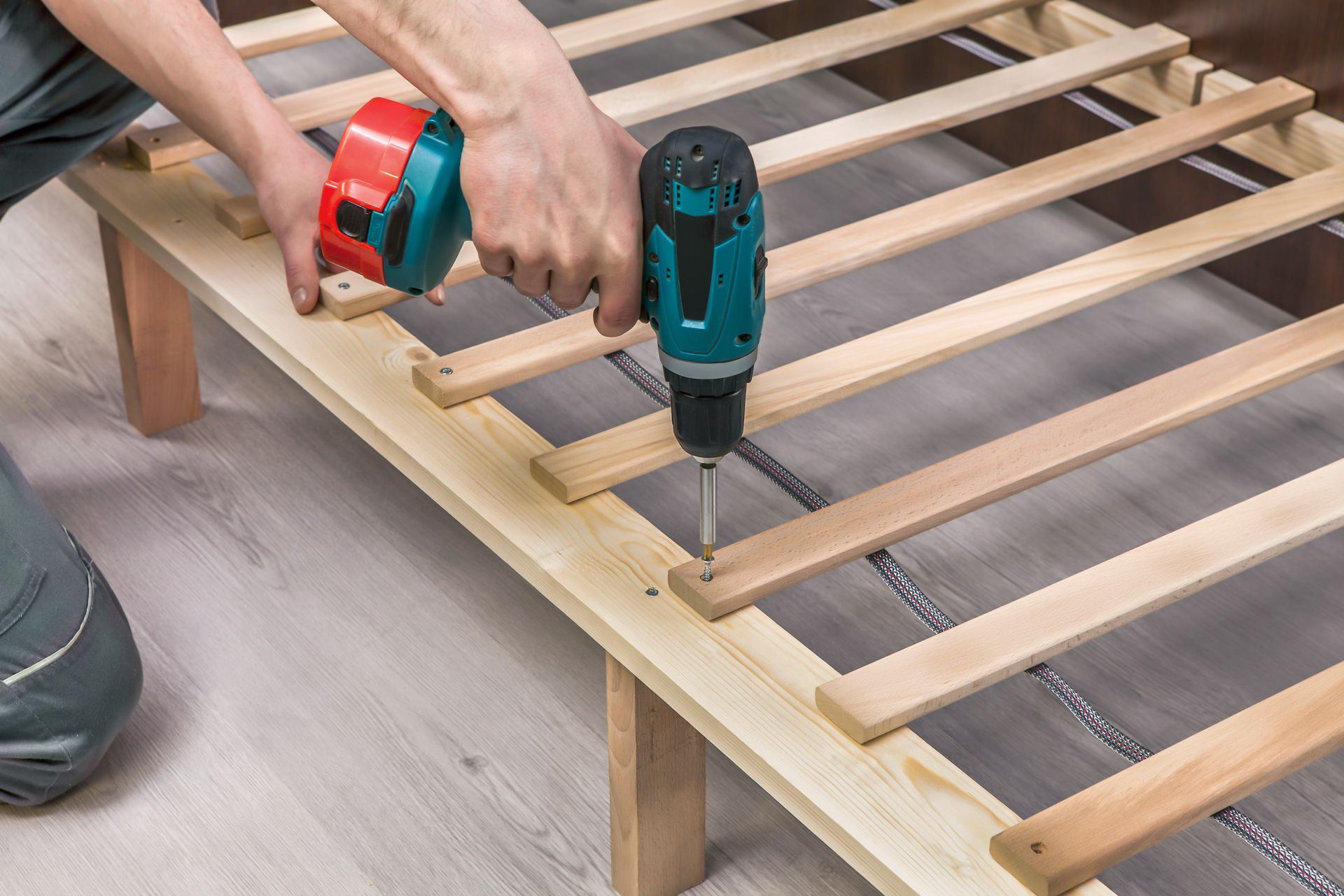 A person is using a drill to screw a screw into a wooden bed frame.