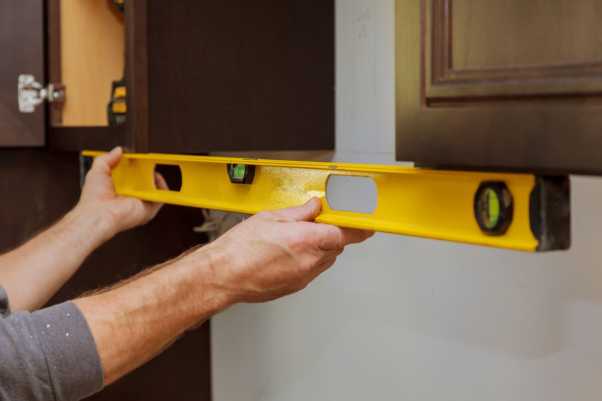 A man is using a level to check the level of a cabinet.