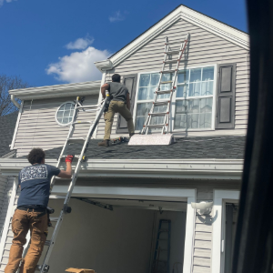 Two workers on ladders painting a house exterior above an open garage.