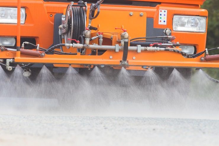 Orange street sweeper spraying water over pavement to control dust