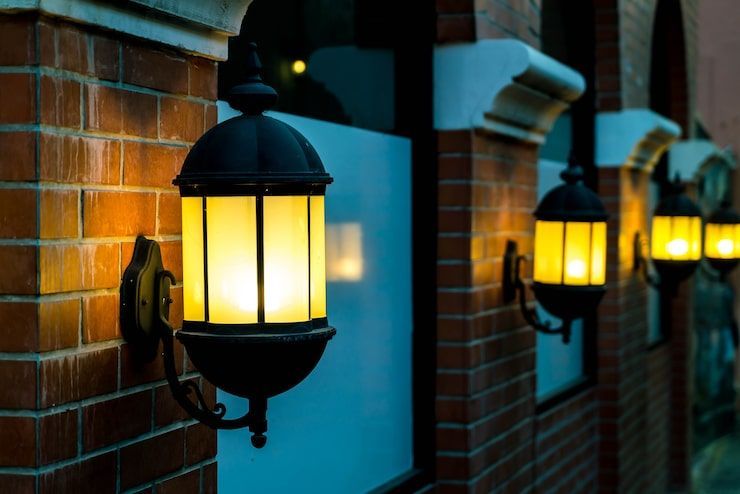 Row of glowing yellow wall lanterns on a brick building at dusk