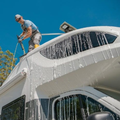 Person washing the roof of a white yacht with a hose under a blue sky