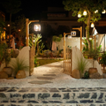 Nighttime garden entrance with stone path, wooden gate, lanterns, and potted plants.
