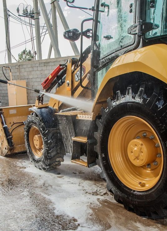 Yellow construction vehicle spraying water on a muddy street beside a wall and utility poles
