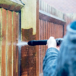 Person pressure-washing a wooden fence with a black spray wand