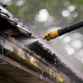 Pressure washer spraying water on a roof gutter close-up