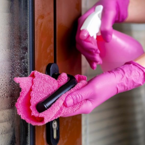 Pink-gloved hands wiping a door handle and lock with a cleaning cloth