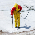 Worker in yellow and red protective gear using a pressure washer on a snowy surface