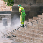 Worker in neon green gear pressure-washing stone steps beside a building.