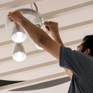Person installing a ceiling light fixture indoors on a white slatted ceiling
