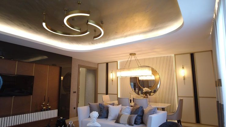 Modern living room with curved ceiling lights, beige sofa, wall TV, and round mirror decor