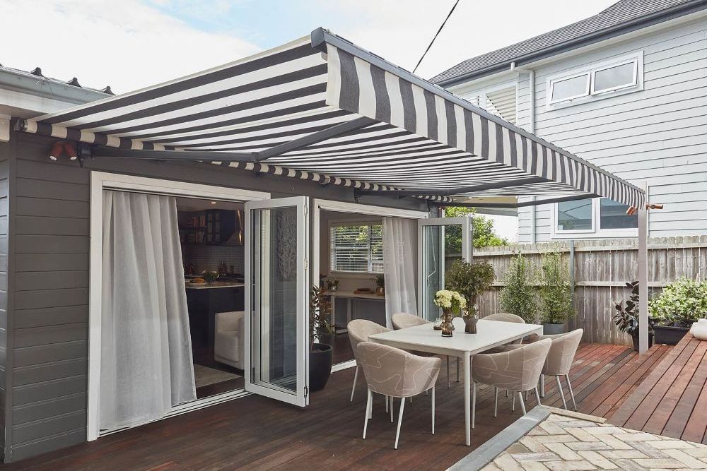 A Patio With a Table and Chairs Under a Striped Awning — Whitsunday Vogue Interiors in Airlie Beach, QLD